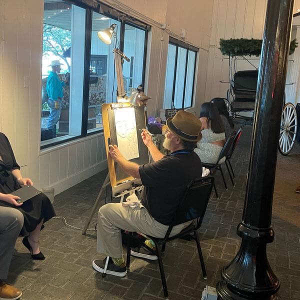 A man sketches a caricature of a woman sitting at a table, capturing her likeness in Dallas, TX