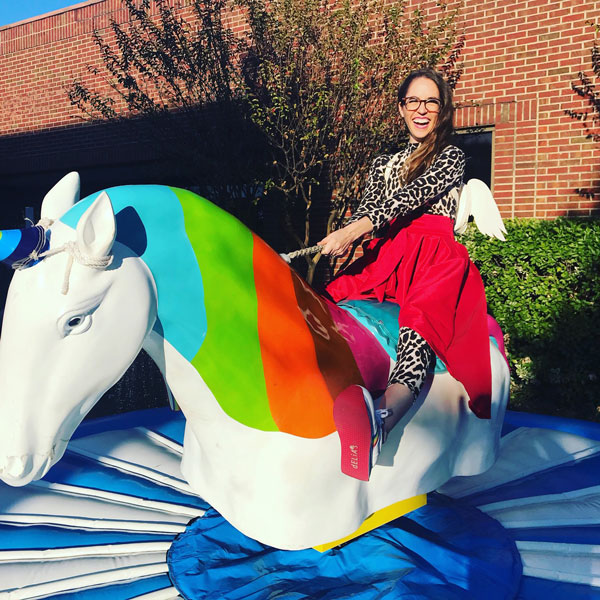 A woman rides a mechanical unicorn in front of a building in Dallas, TX